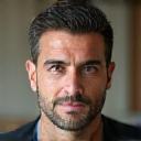 Πορτρέτο του Γιάννη Κώστα, ενός άνδρα μεσήλικα με ήρεμο πρόσωπο και εκφραστικά μάτια, που αποπνέει ηρεμία και ενσυναίσθηση.